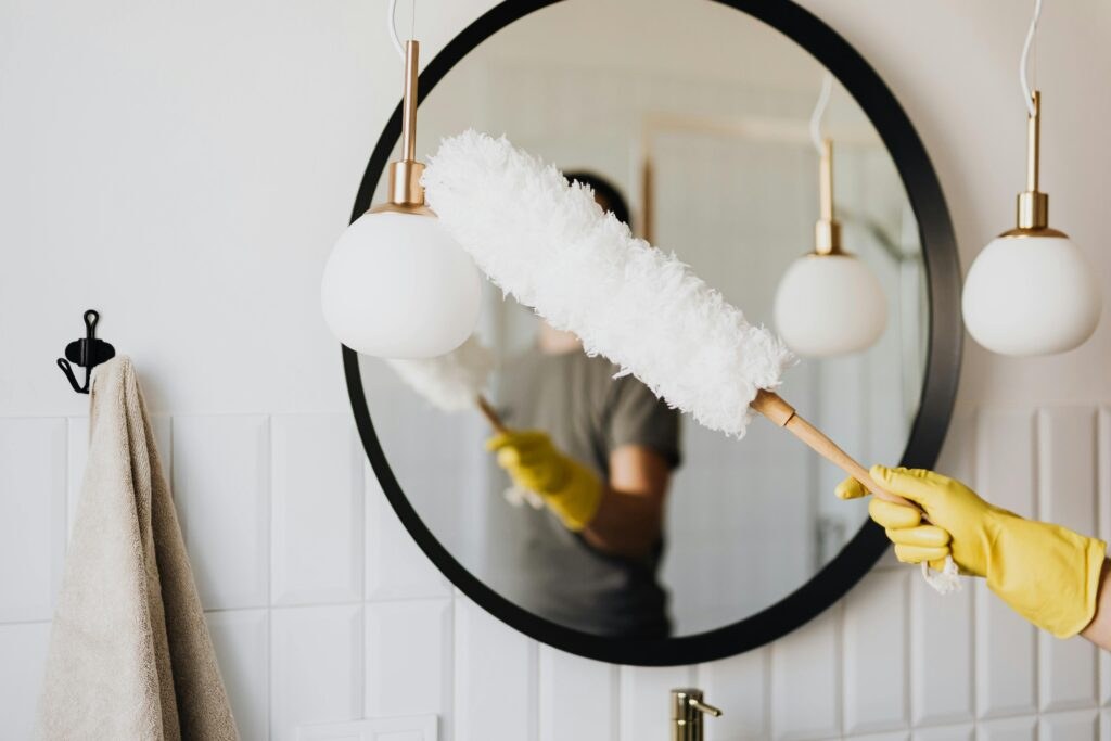 Dusting a round mirror with a yellow-gloved hand