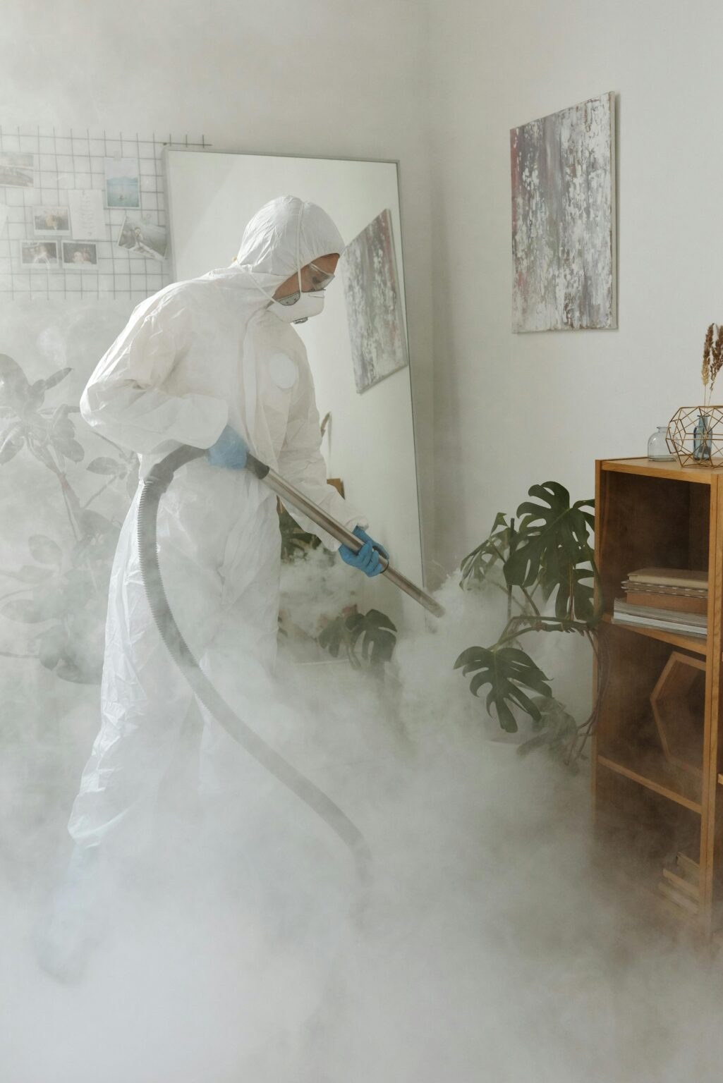 Technician in a protective suit spraying disinfectant through a room